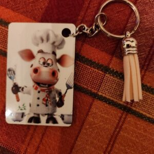 Cute cow chef keychain with a tassel on a checkered cloth.