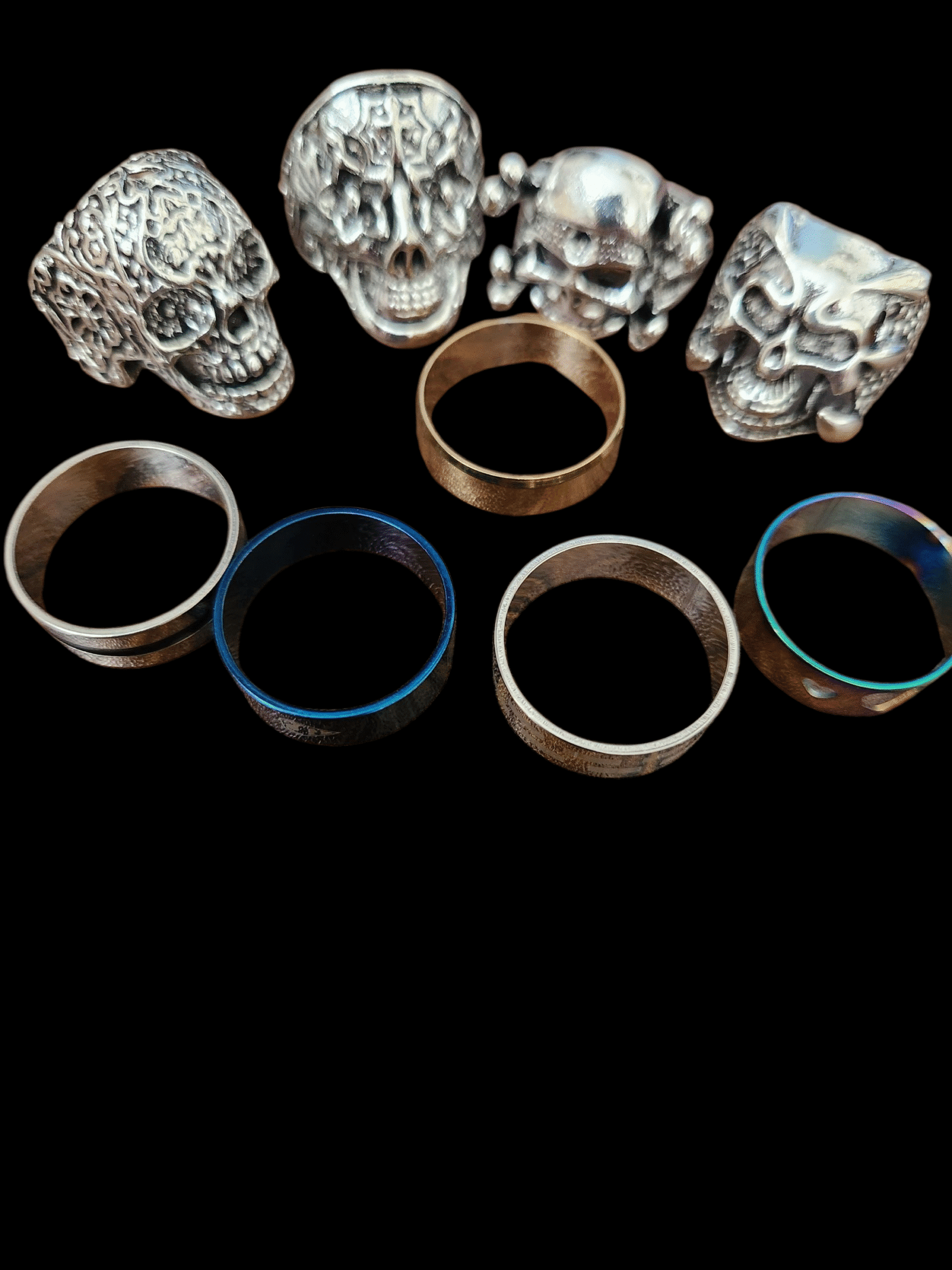 Five metal rings with a row of three silver skull figurines on a black background.