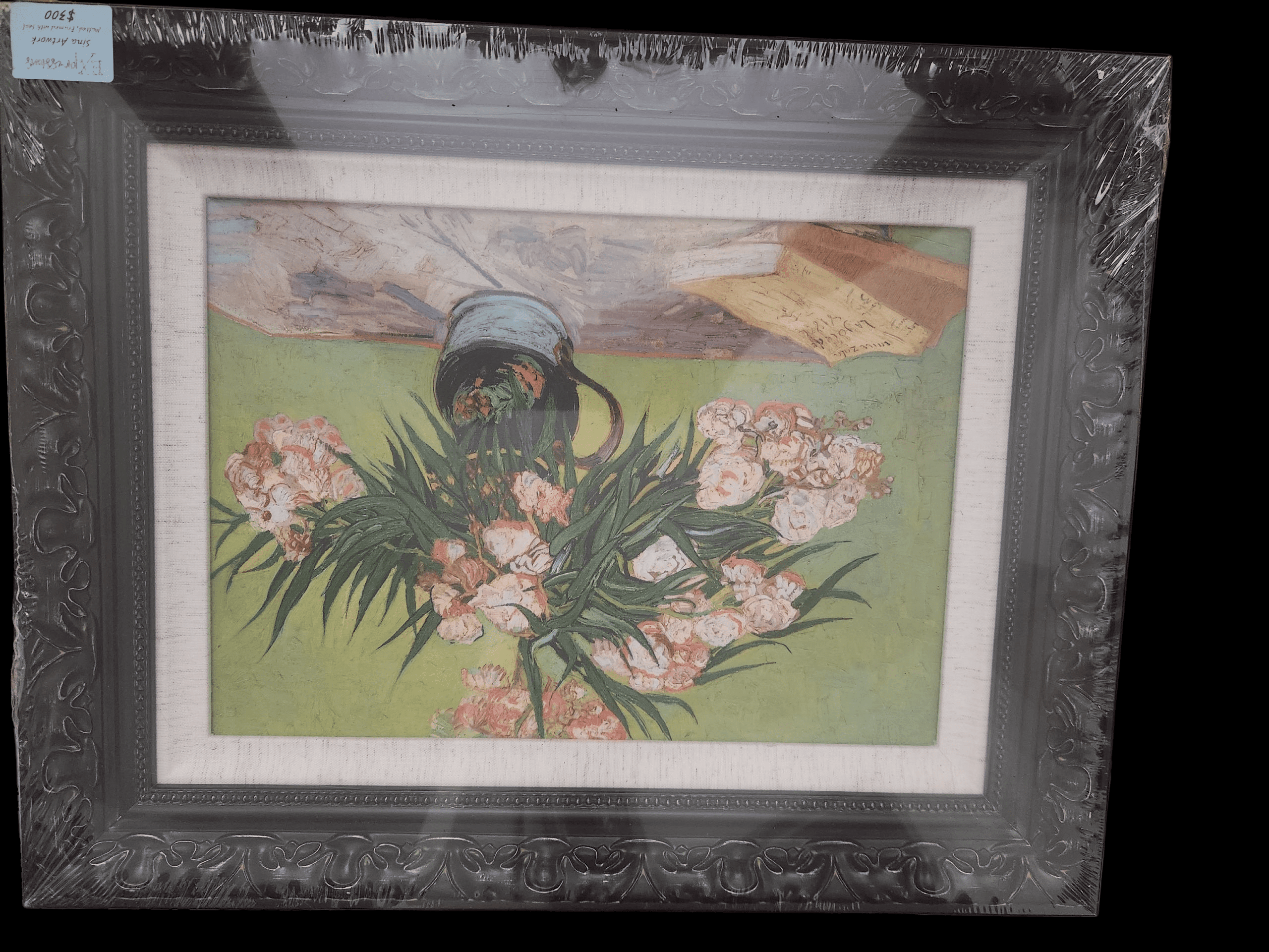 A framed painting of white flowers and green leaves on a table.