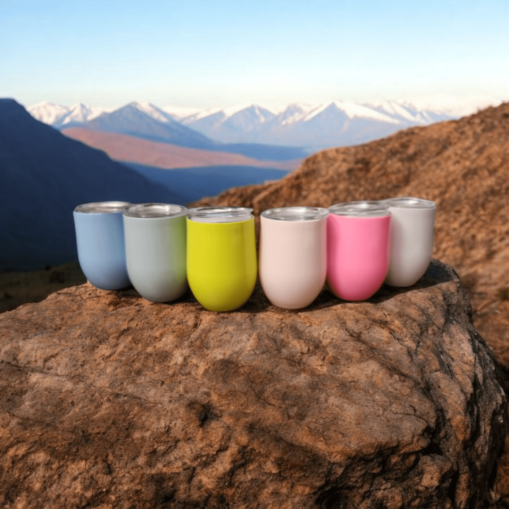 Colorful cups lined up on a rocky mountain ledge at sunrise.